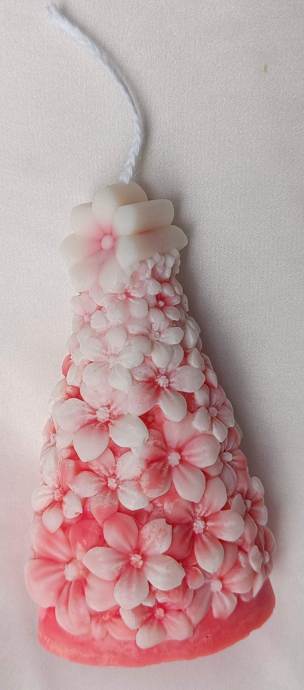 Detalle frontal de vela Árbol de Navidad con flores en relieve y tonos blancos y rosados, decoración festiva.