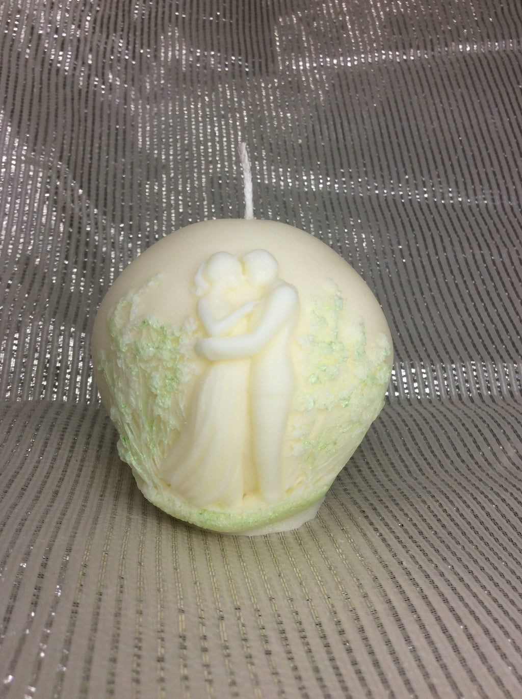 Vela artesanal redonda para aniversario con figura de novios y detalles verdes.