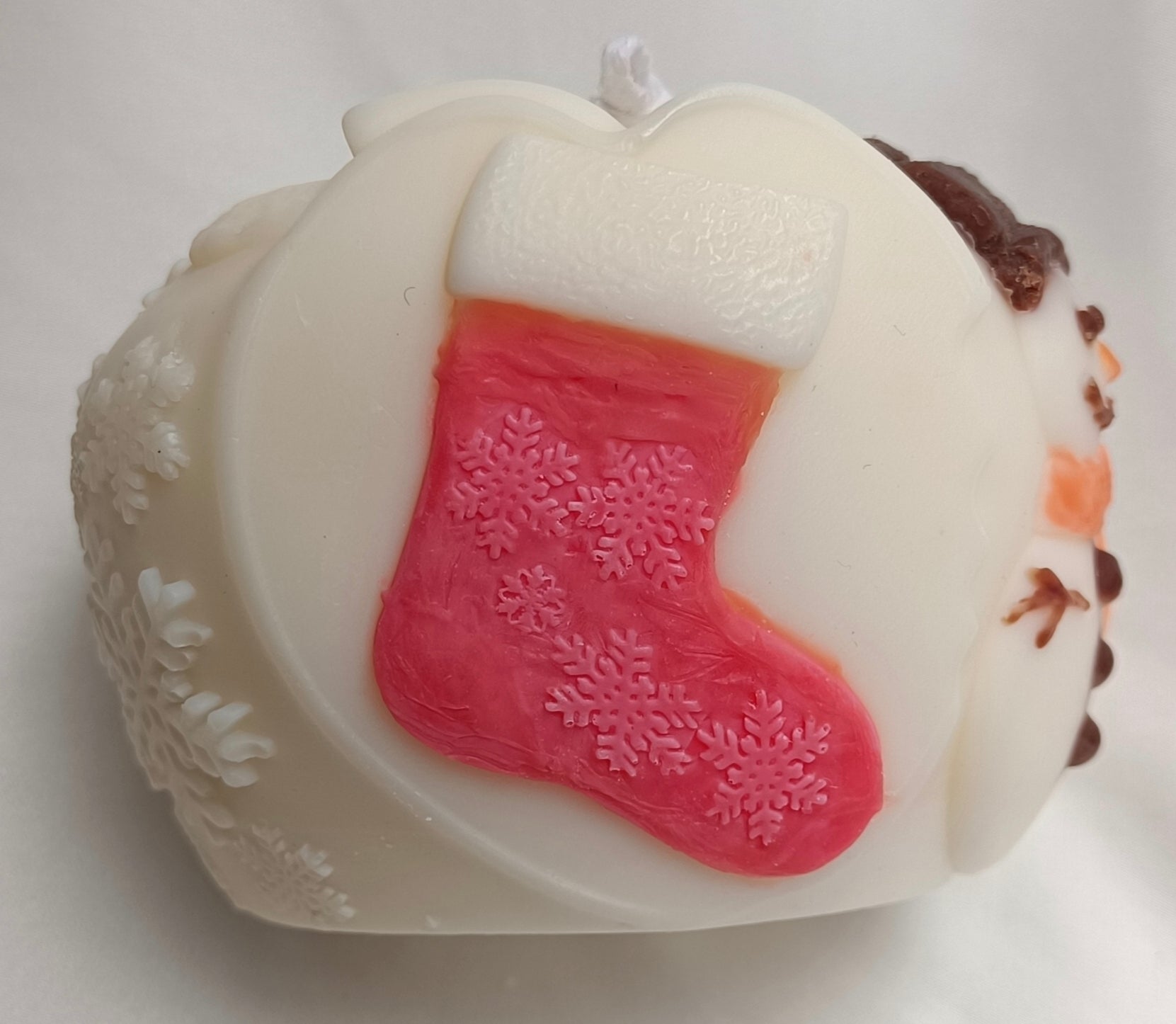 Detalle de vela artesanal Bola de Navidad, mostrando el relieve tallado de muñeco de nieve y calcetín festivo.