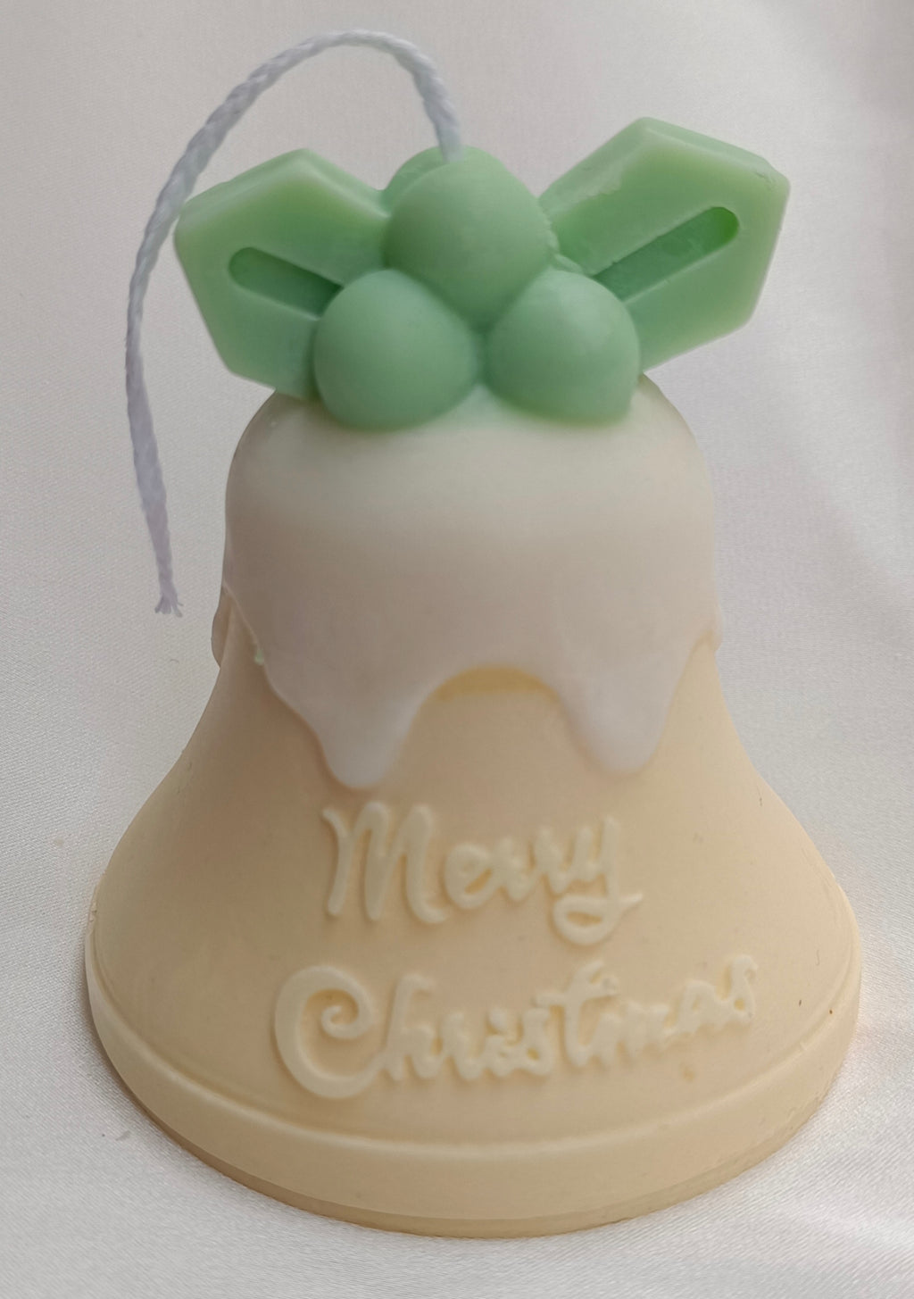 Vela artesanal Campana de Navidad con acebo verde, glaseado blanco y mensaje "Merry Christmas" tallado.