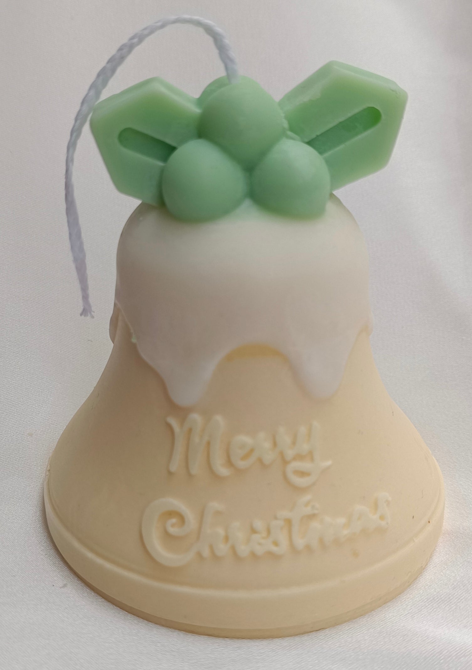 Vela artesanal Campana de Navidad con acebo verde, glaseado blanco y mensaje "Merry Christmas" tallado.