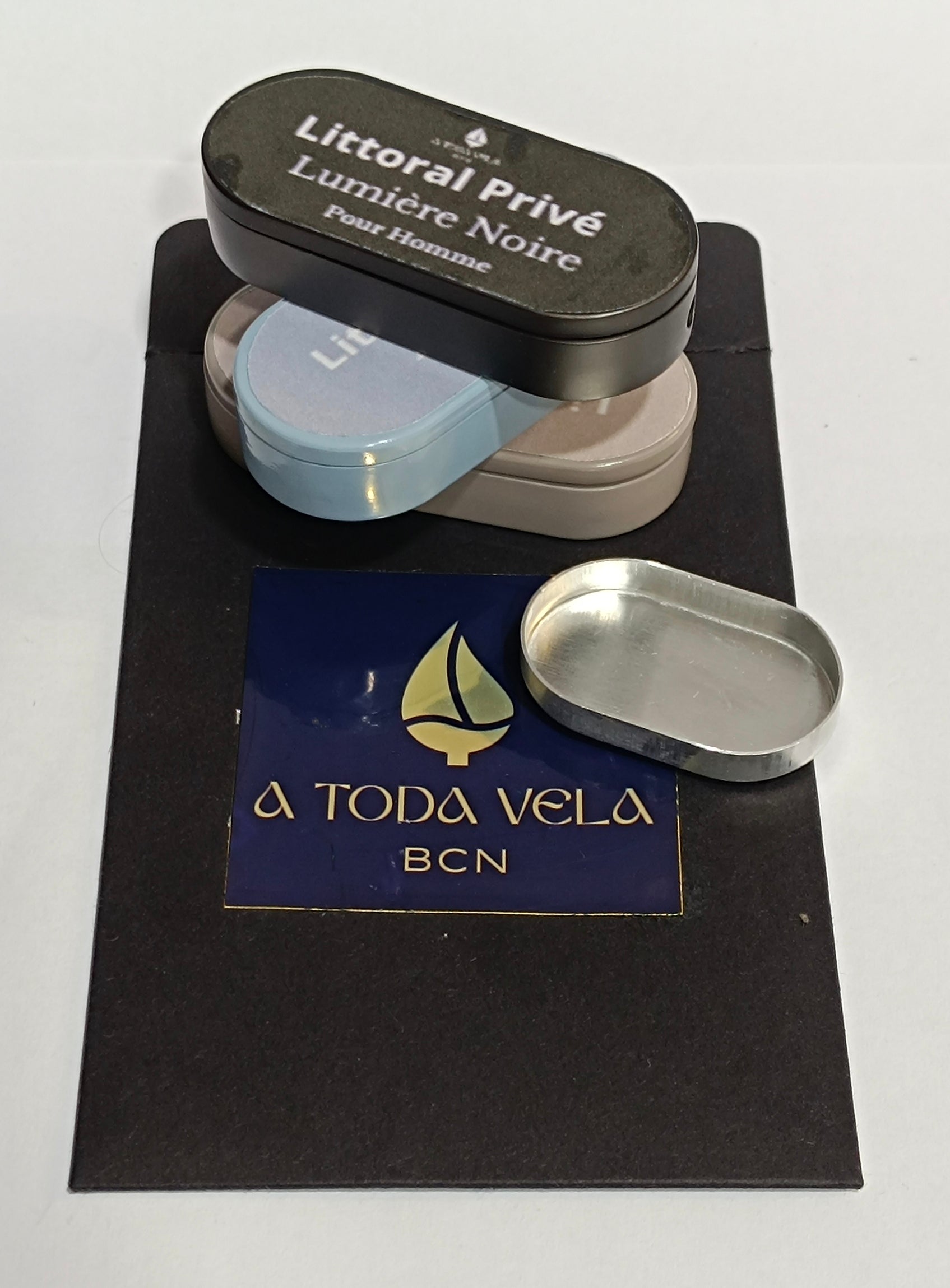 Recambio de perfume sólido Aura Terra y otros estuches Litoral Privé apilados, mostrando un envase vacío listo para la recarga sostenible.