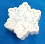 Vela artesanal blanca en forma de copo de nieve sobre un fondo azul, con la mecha encendida visible.