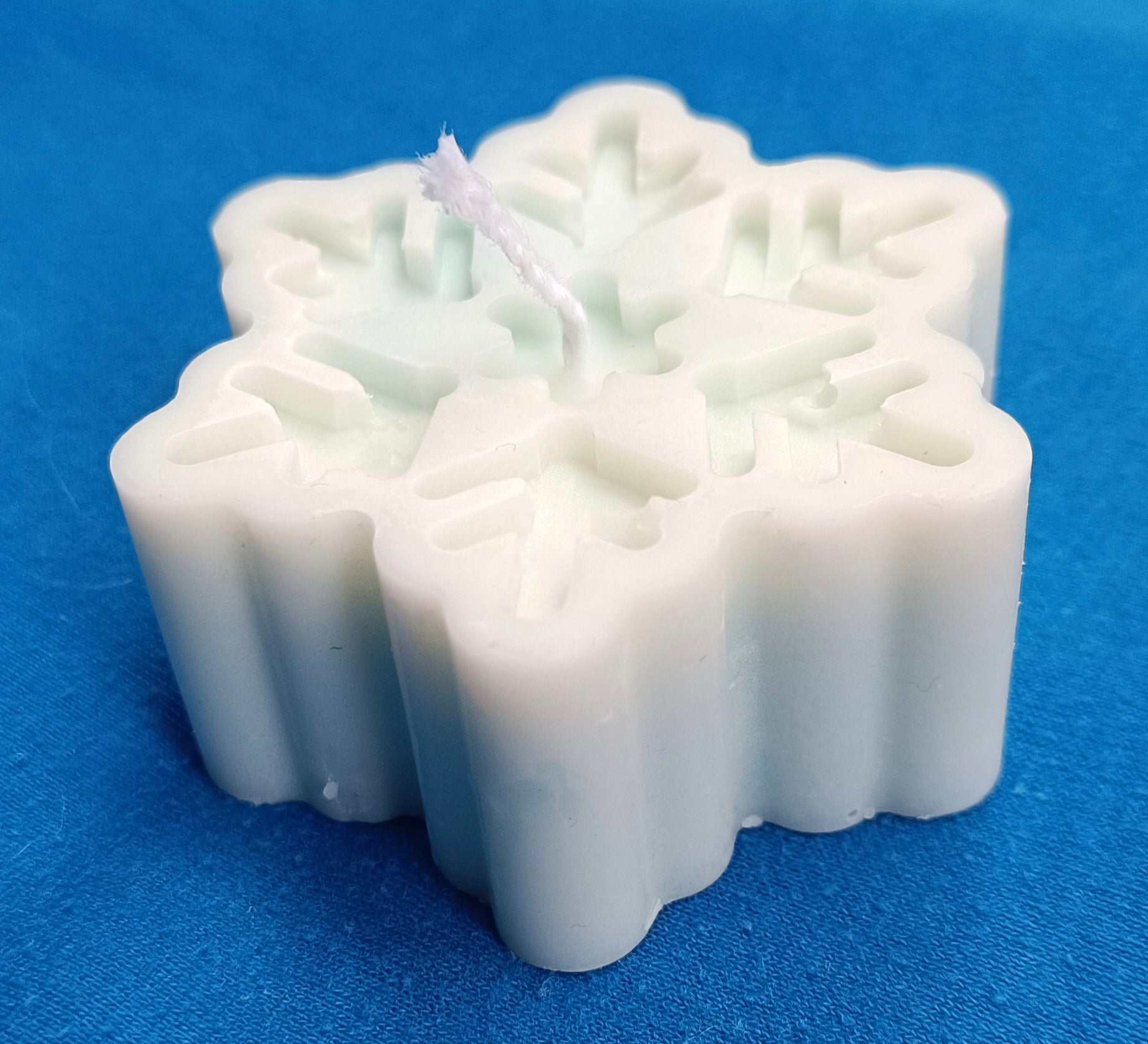 Vela artesanal blanca en forma de copo de nieve vista desde arriba sobre un fondo azul, mostrando los detalles del diseño.