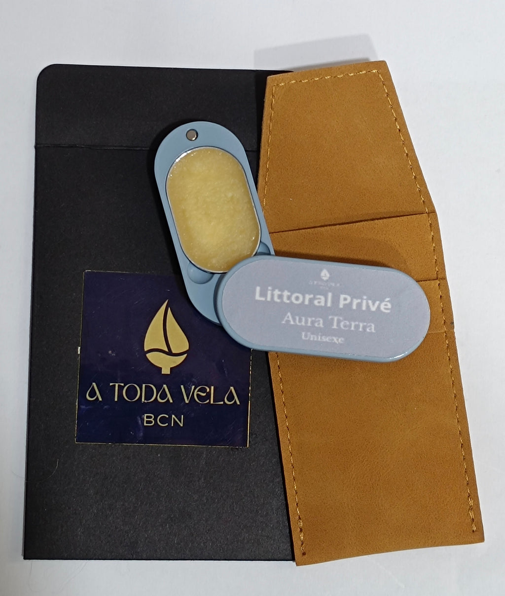 Perfume sólido natural 'Aura Terra' (unisex) en su estuche metálico azul abierto, mostrando la cera perfumada, junto a su funda de antelina.