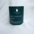 Primer plano de la vela de cera de soja 100% ecológica A Toda Vela BCN, colección Rumbo al Deseo, en recipiente color verde oscuro. Se aprecia el logo de A TODA VELA BCN y el texto "LOVE YOUR LIFE ENJOY" y la información "300g/10.6oz SCENTED CANDLE / SOY WAX". El envase elegante resalta la fragancia Oriental-Floral de Rosa Damasco y Vainilla Bourbon.