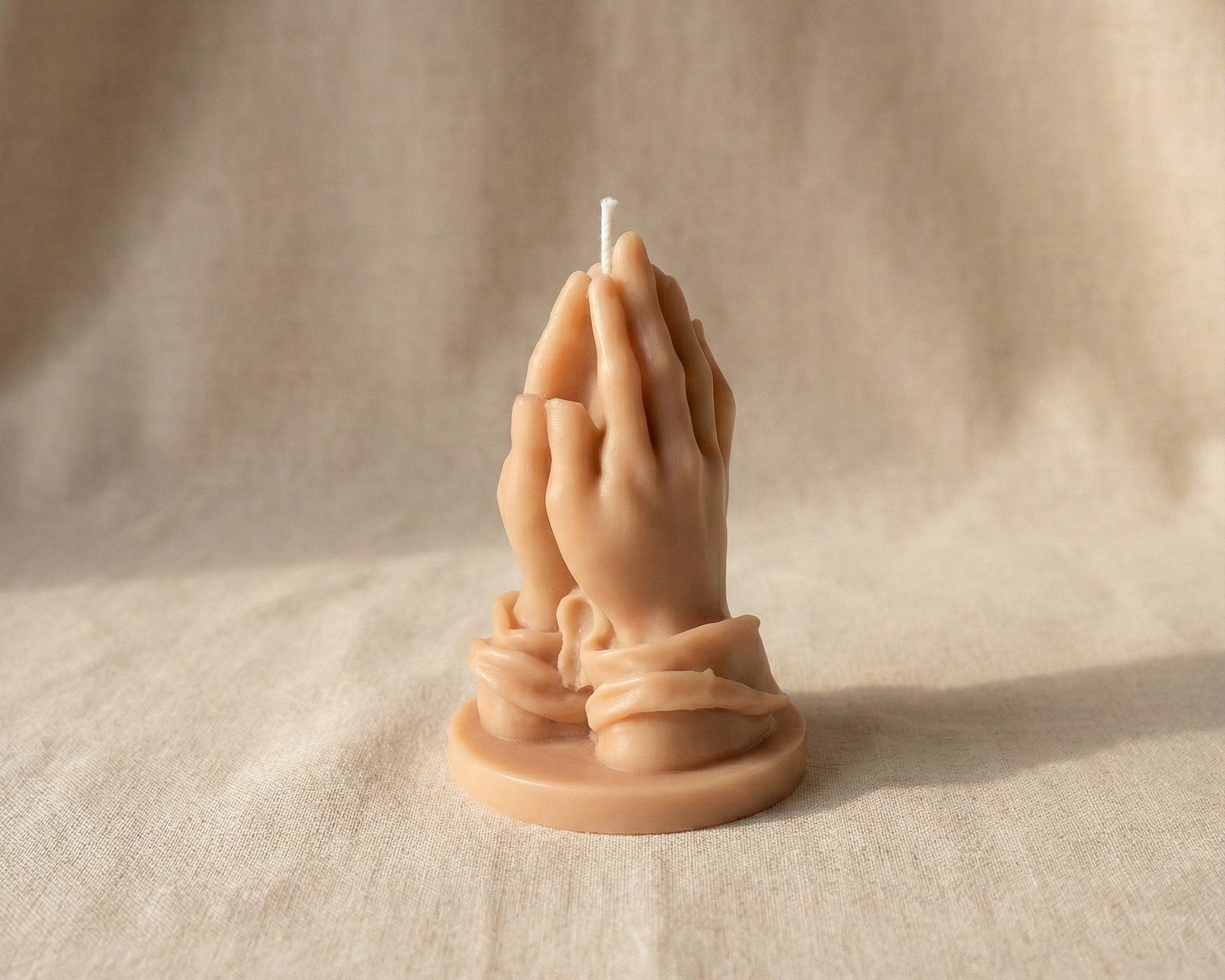 Vela escultural de cera con forma de manos rezando en tono piel beige.
