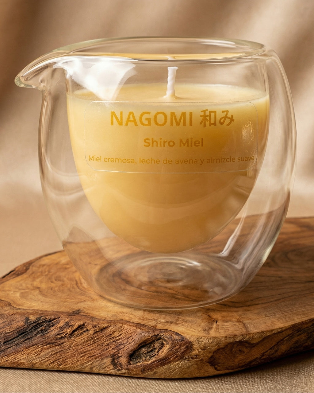 Vela aromática NAGOMI Shiro Miel en vaso de cristal de doble pared, con aroma de miel cremosa, leche de avena y almizcle suave, sobre una base de madera rústica y fondo beige.