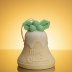 Vela Campana Navidad Acebo en tono crema y verde, con mensaje grabado "Merry Christmas", sobre un fondo dorado claro.