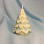 Vela decorativa en forma de árbol de Navidad de cera blanca, con detalles de copos de nieve azules, sobre un fondo de tela azul claro.