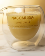 Vela aromática en vaso de cristal de doble pared con etiqueta "Amai Daichi" y flores secas decorativas, colocada sobre una base de mármol con un fondo dorado suave.