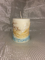 Vela Papá Noel Trineo, cilíndrica, relieve 3D pintado a mano en tonos dorados y azules sobre fondo plateado.