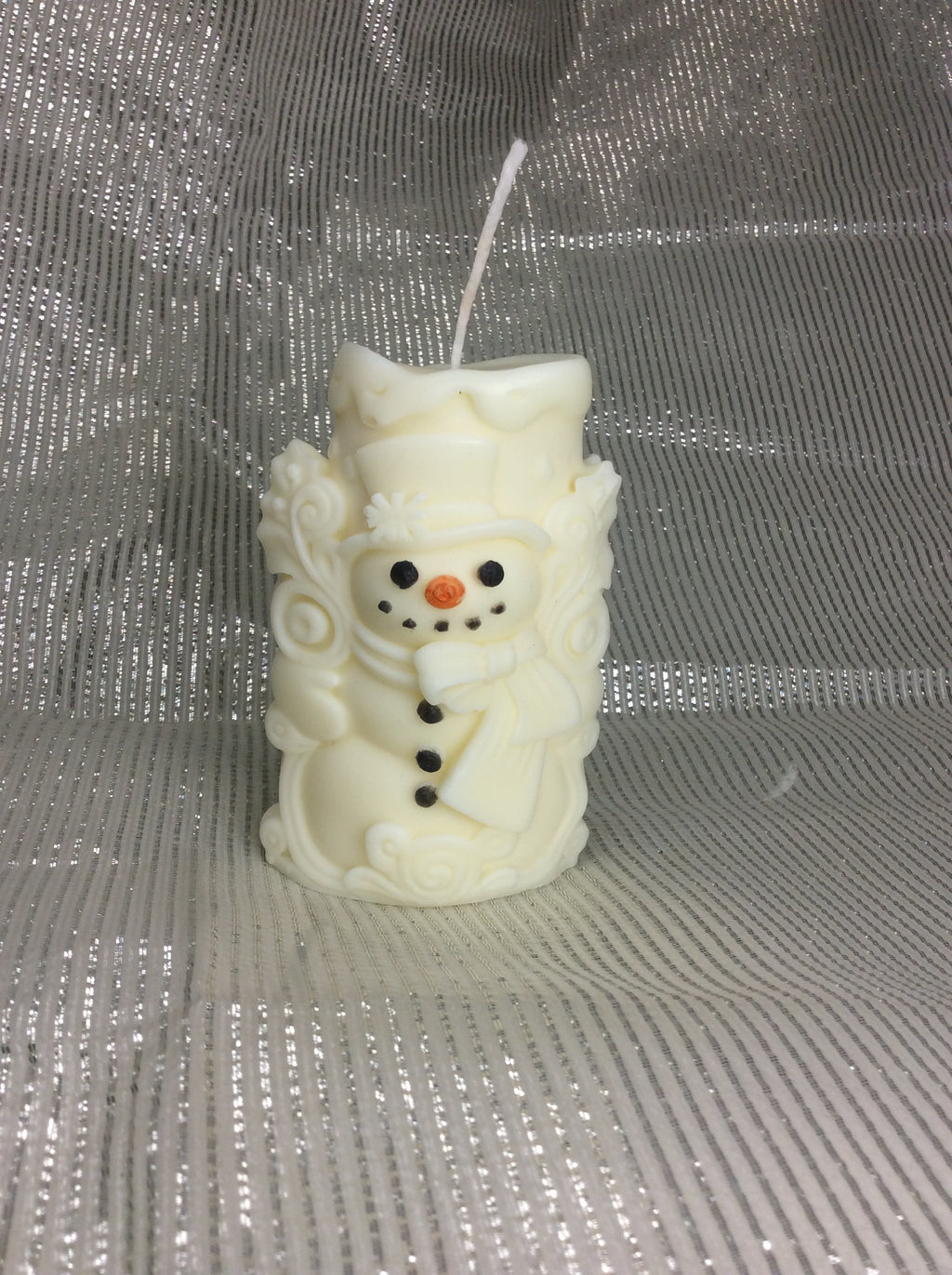 Vela aromática de muñeco de nieve con relieve 3D sobre fondo plateado.