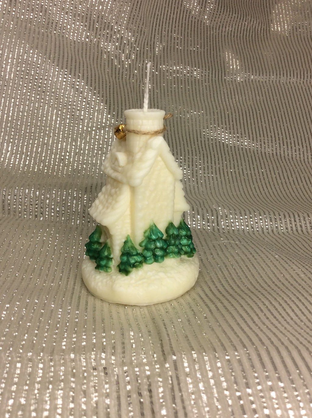 Vela artesanal de iglesia navideña con pinos verdes pintados a mano sobre fondo plateado.