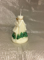 Vela artesanal de iglesia navideña con pinos verdes pintados a mano sobre fondo plateado.