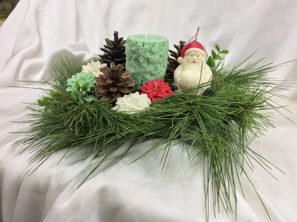 Vela artesanal de Papá Noel junto a una vela verde con relieve y piñas