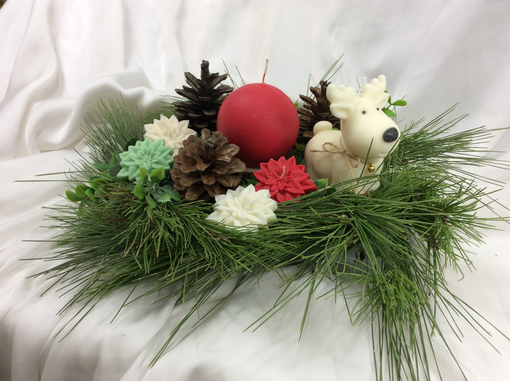 Arreglo de Navidad con vela de reno, piñas y una vela roja esférica.