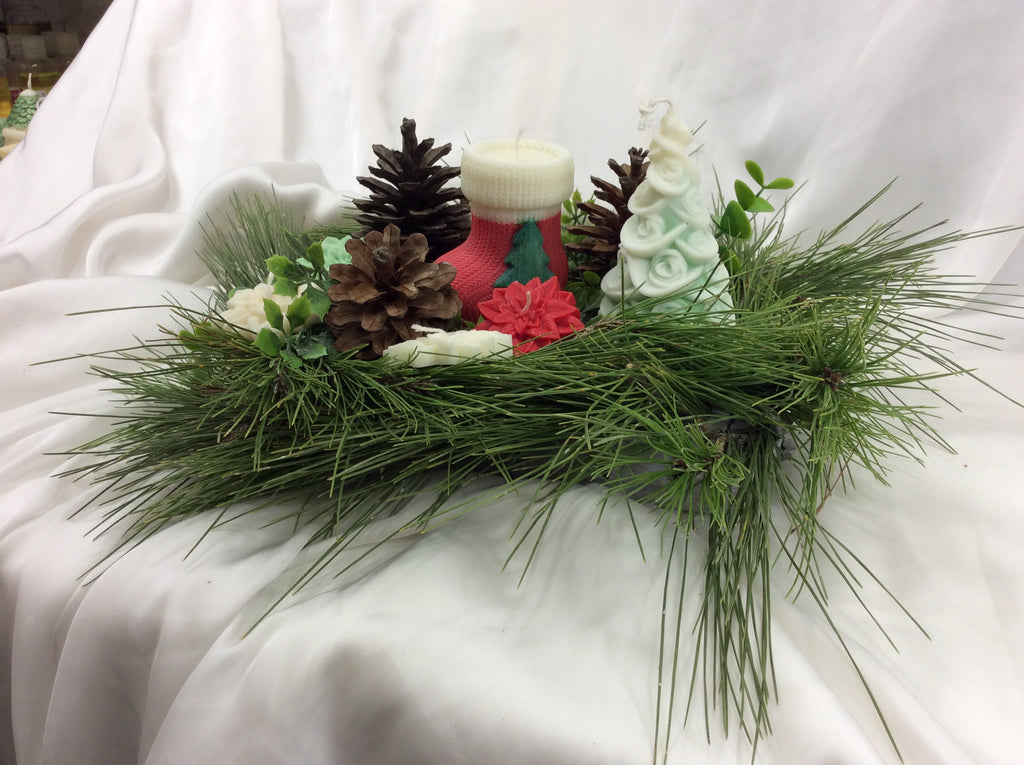 Vela con forma de calcetín de Navidad junto a un pino de cera y piñas.