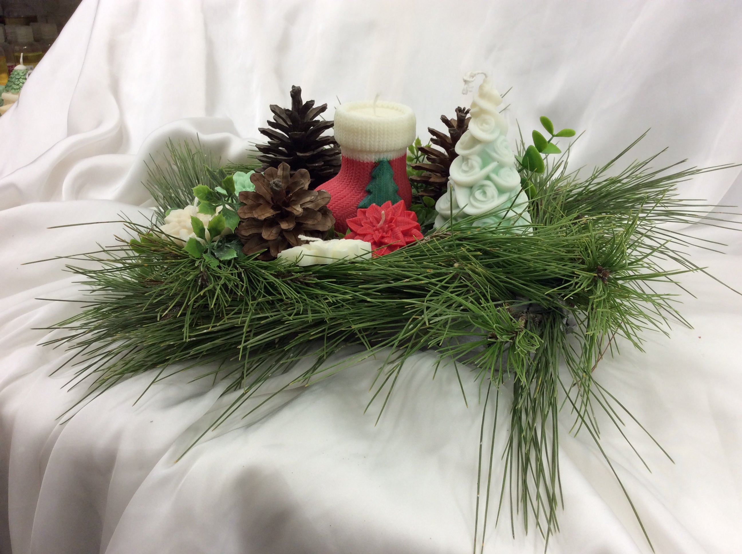 Vela con forma de calcetín de Navidad junto a un pino de cera y piñas.