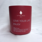 Primer plano del envase de la vela de lujo Rumbo al Alba de A Toda Vela BCN. El logo de la marca está visible sobre el vibrante color rojo del recipiente. El producto está hecho a mano en Barcelona con cera vegetal pura, ideal para un ambiente fresco, limpio y sereno. La fragancia principal es Bergamota y Corazón Floral (Azahar).