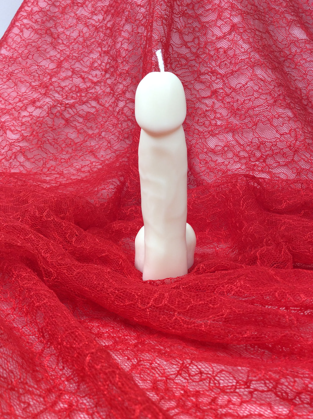 Vela con forma de pene para regalo de broma sobre encaje rojo.