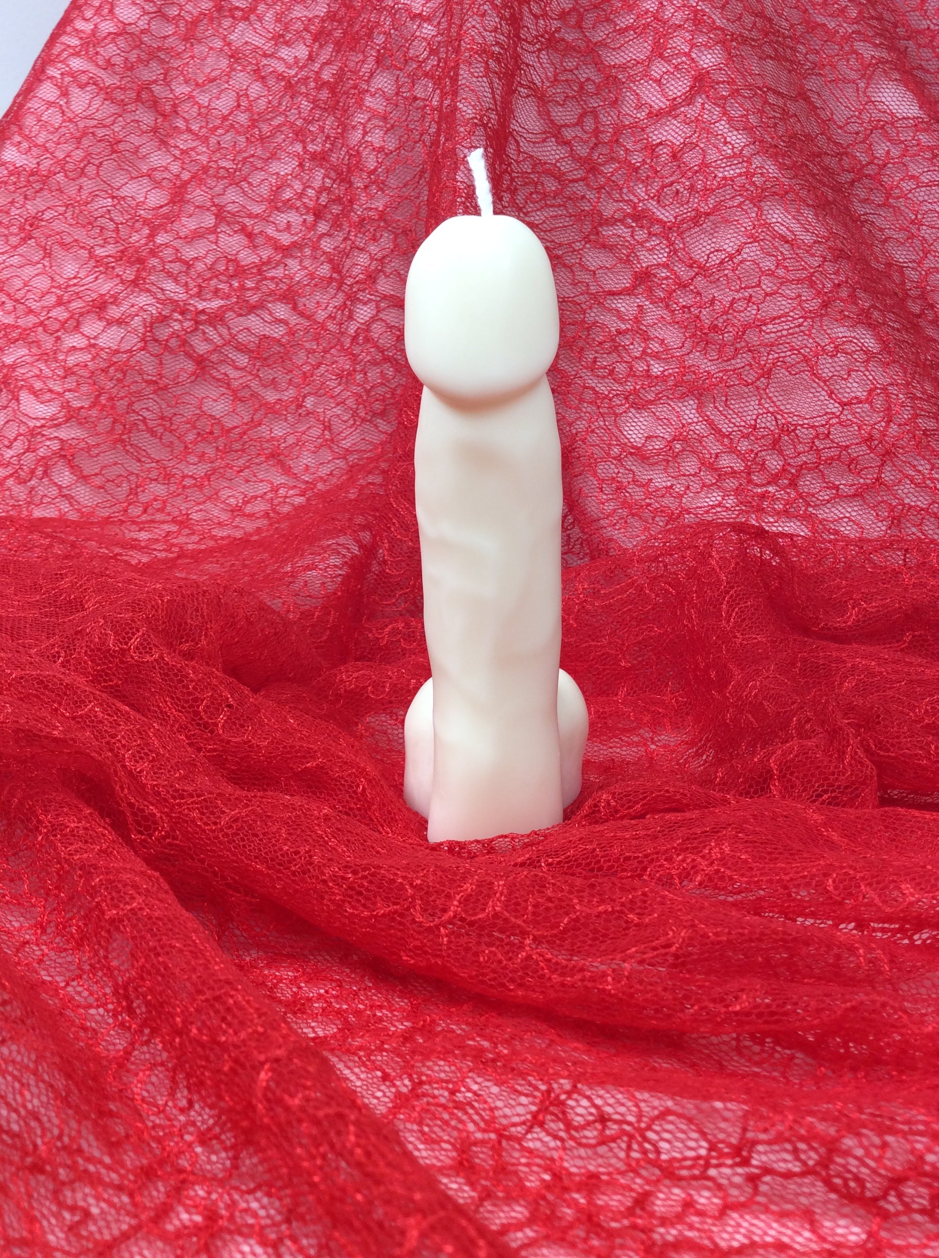 Vela con forma de pene para regalo de broma sobre encaje rojo.