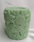 Vela artesanal cilíndrica verde con relieve de muñeco de nieve sonriente y copos, decoración navideña.