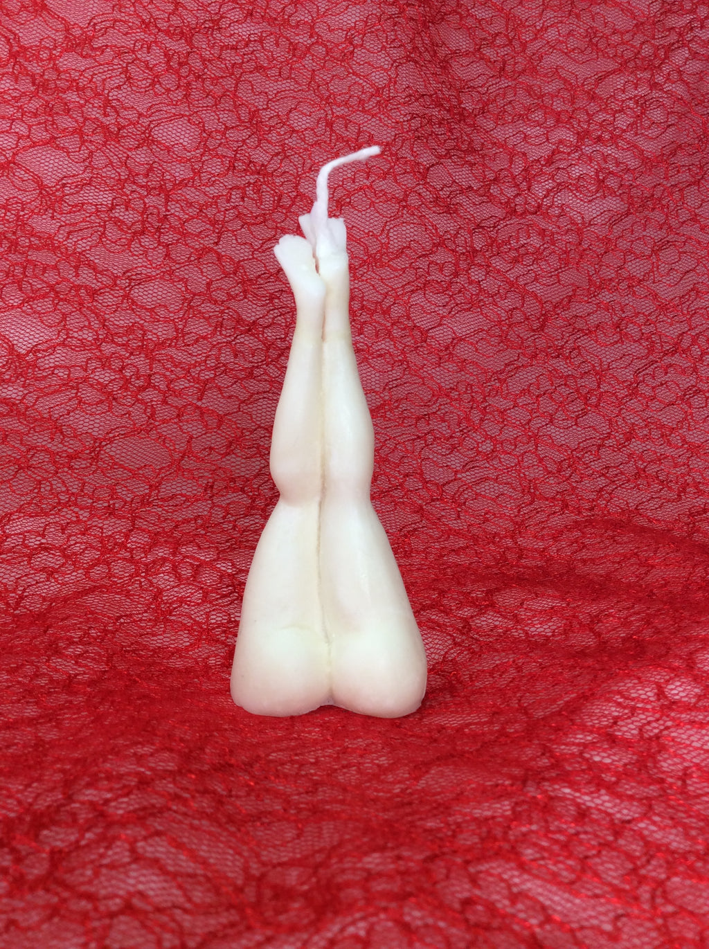 Vela erótica con forma de piernas de mujer sobre fondo de encaje rojo.