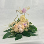 Arreglo de velas de cera ecológica, Grandeza Eterna. Figura religiosa central rodeada de hojas de eucalipto y flores de cera pastel. Souvenir de lujo y arte.