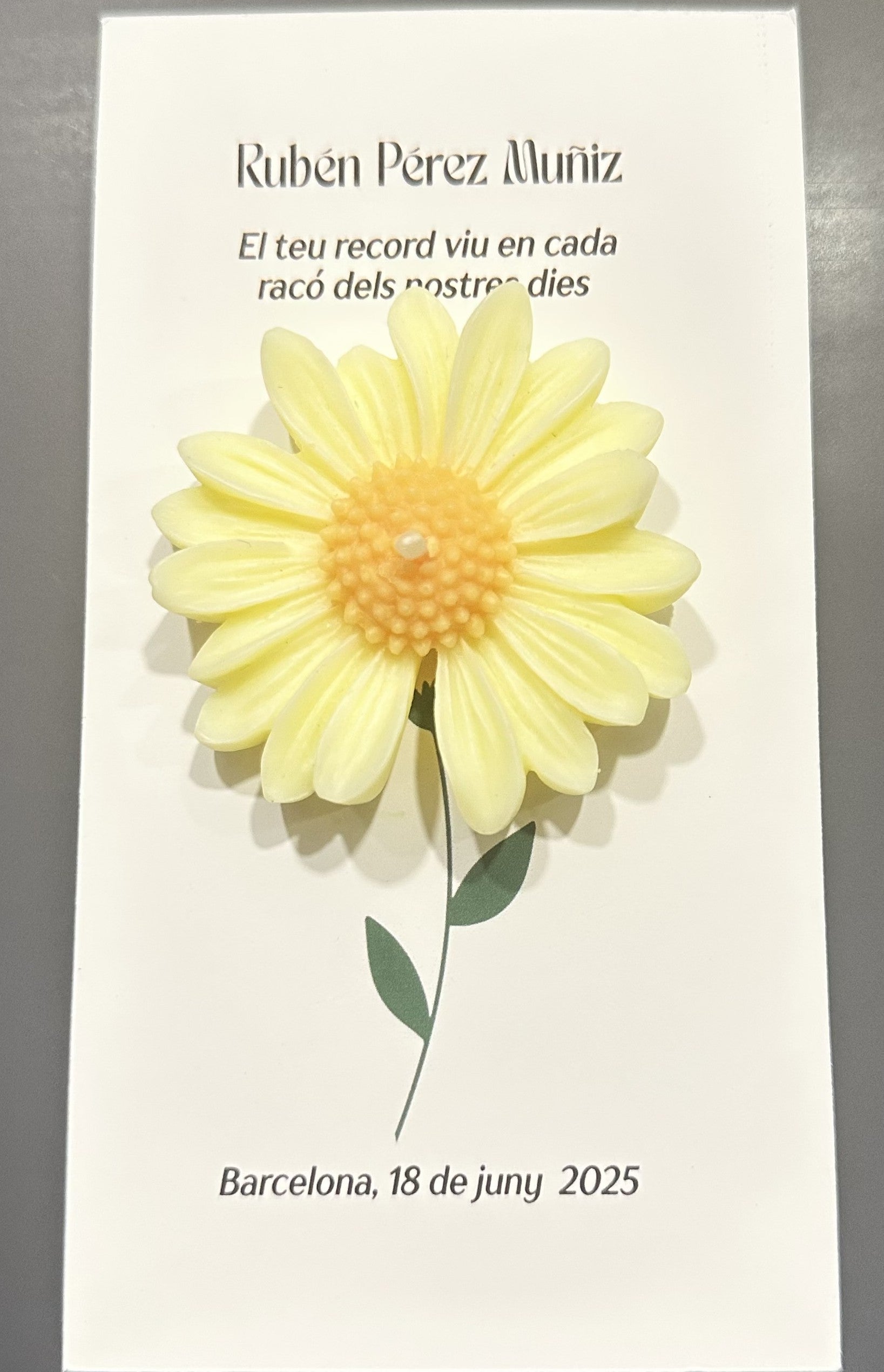 Vela margarita amarilla con centro perlado, adherida a una tarjeta recordatorio personalizada con el nombre