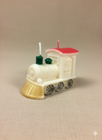 Vela Navidad Tren Locomotora pintada a mano, con detalles en rojo, dorado y verde, sobre un fondo beige suave, realzando su brillo