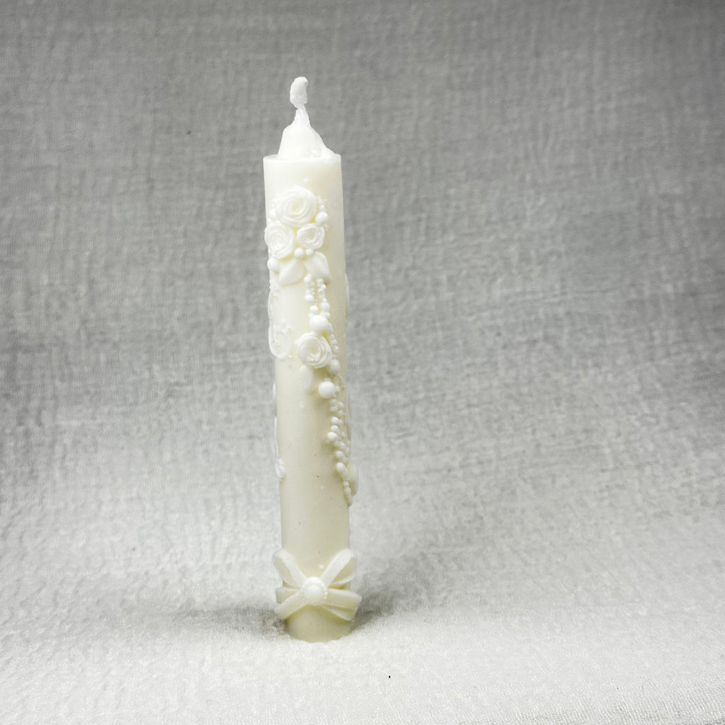 Cirio de bautizo ecológico de color rosa pálido, decorado con relieves de flores y un lazo.