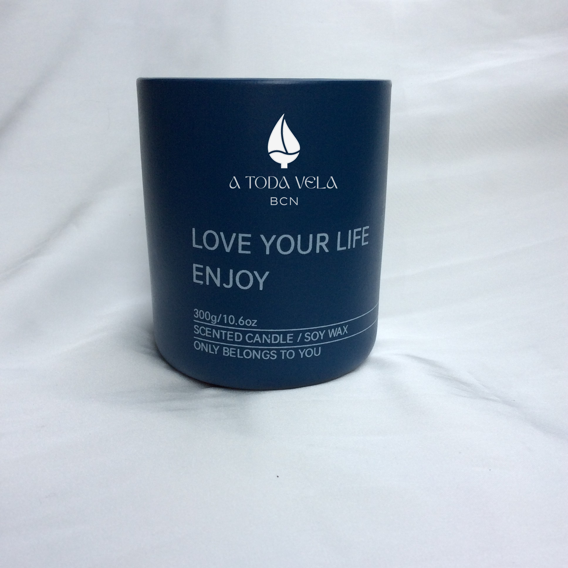 Primer plano de la vela ecológica A Toda Vela BCN Rumbo al Horizonte en tarro azul marino. Se distinguen el logo y el texto "SCENTED CANDLE / SOY WAX 300g". La vela de cera vegetal 100% ecológica y mecha de algodón representa la fragancia fresca, mineral y profunda inspirada en el mar, con notas de Ámbar Solar y Cedro.