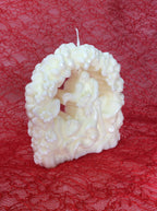 Detalle de la vela de boda con pareja bajo un arco de flores sobre fondo rojo.