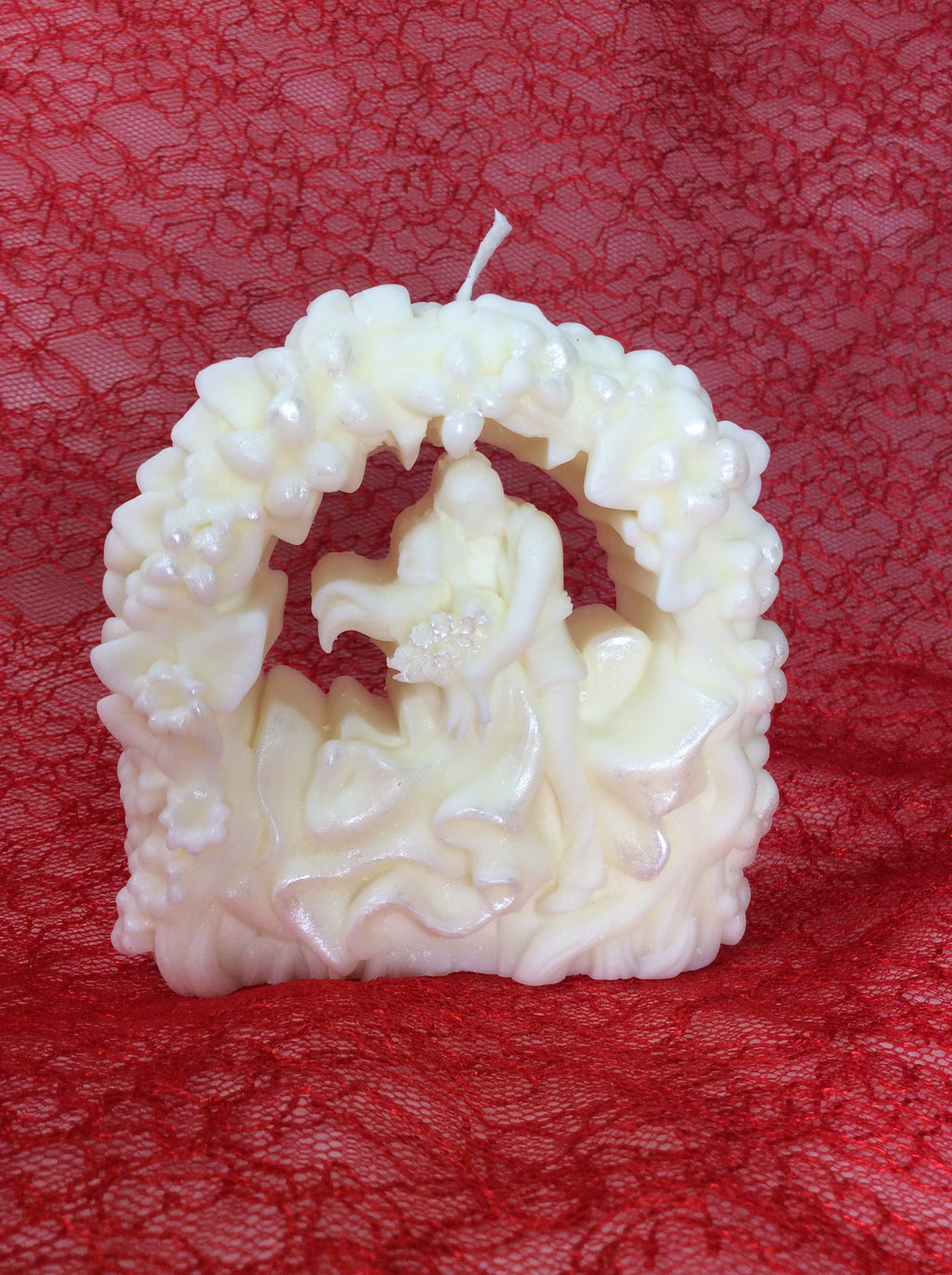 Vela de boda artesanal con novios bajo un arco floral y acabado nacarado.