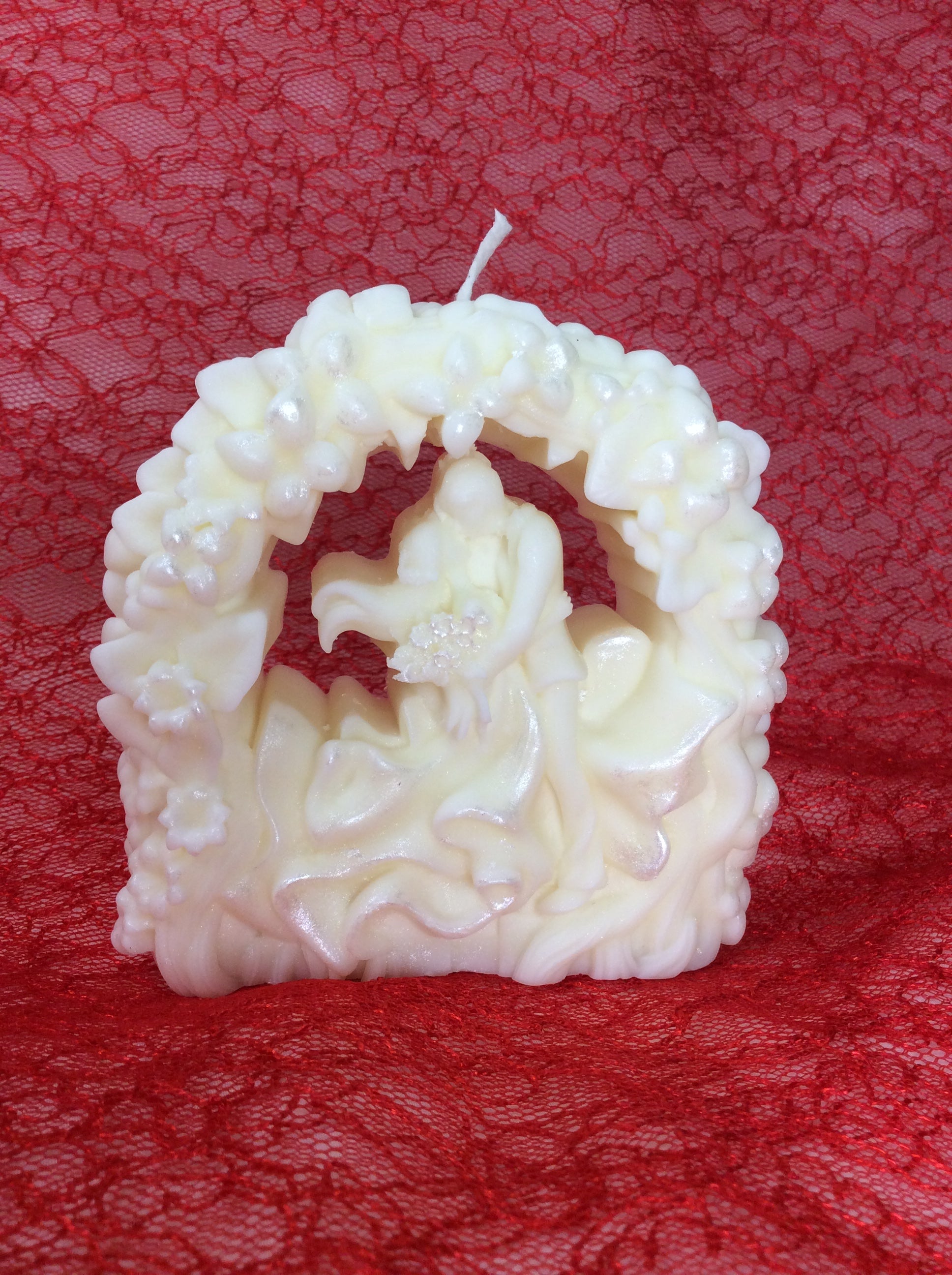 Vela de boda artesanal con novios bajo un arco floral y acabado nacarado.